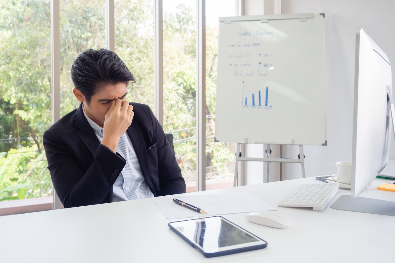 Businessman sit at a desk in an office green trees. He with his hand holding his face feel sad, worry, fatigue, frustration, irritability, failure after failure.